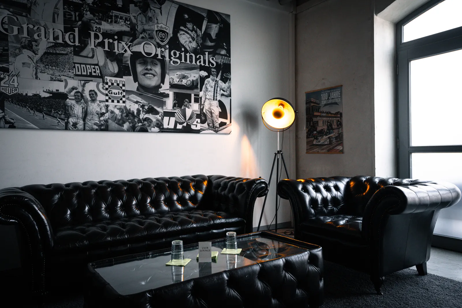 Club Lounge der Oldtimerfabrik Classic mit schwarzen Chesterfield Sofas und Grand Prix Originals Collage