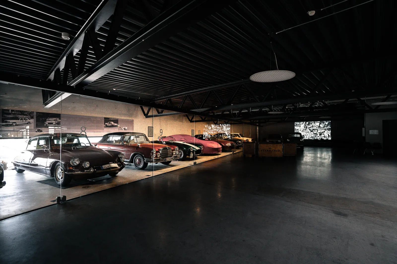 Reihe klassischer Fahrzeuge hinter Glas in der dunklen Ausstellungshalle der Oldtimerfabrik Classic
